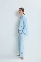 Conjunto de pijama celeste a rayas verticales blancas, compuesto por una camisa de manga larga con cuello mao y botones, y un pantalón de corte recto. La camisa y el pantalón tienen bordados de corazones, soles y otros motivos.