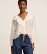 Blusa color blanco confeccionada en voile, de mangas largas con elástico en los puños, cuello en V con volado y lazo con adornos metalizados.