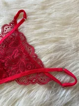 Conjunto de lencería rojo de encaje, compuesto por un bralette con breteles regulables, una tanga regulable con corte media less y un portaligas con volados.