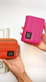 Billetera corta con cierre alrededor y tapa, confeccionada en tela capitoneada. Incluye varias reparticiones con tarjeteros y bolsillos internos, y una correa de mano desmontable. Disponible en negro, rojo y dorado.