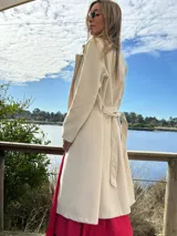 Abrigo trench color crudo, de paño fino con dibujo en sarga, forrado, con cuello solapa, doble botonadura y cinturón con lazada.