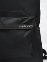 Mochila con estampado tie-dye en tonos grises y blancos, con bolsillo frontal con cierre y logo "Forum Active" estampado. Incluye bolsillo lateral de red para botella.