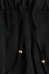 Pantalón negro de piernas anchas con bolsillos laterales, cintura elástica y cordón de ajuste con cuentas decorativas en los extremos.