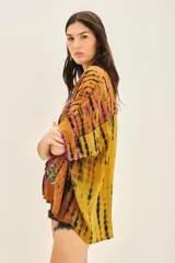 Camisa de manga corta con cuello mao y calce amplio, confeccionada en viscosa con teñido tie-dye en tonos mostaza, negro y violeta. Presenta bordados florales con mostacillas, lentejuelas y canutillos en tonos turquesa y dorado en la parte delantera.