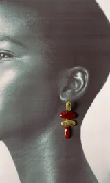 Aros colgantes con diseño de tres piezas: una pieza superior dorada irregular, una pieza central ovalada color bordó, una pieza intermedia dorada con textura y una pieza inferior alargada color bordó.