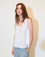 Top sin mangas blanco de lino, con escote redondo, corte en A, ruedo asimétrico y recortes laterales.