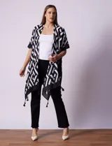 Kimono tejido con estampado geométrico en blanco y negro, ruedo con borlas y composición 100% poliéster.