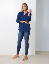 Blusa de gasa color beige, con cuello a la base y escote en V. Manga larga con presilla y botón para ajustar el largo.