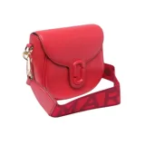 Cartera bandolera Marc Jacobs modelo The Saddle Bag, color negro, de cuero, con cierre de solapa con broche magnético y logo de la marca en el frente. Incluye correa ancha de tela con el nombre de la marca en blanco y negro.