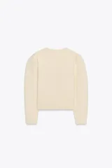Chaqueta color crema de punto con cuello redondo, manga larga, corte entallado, bajo asimétrico y cierre frontal con botones marrones.