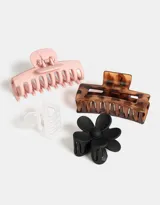 Set de cuatro broches para el pelo de diferentes formas: dos broches rectangulares, uno con diseño carey y otro rosa pastel; un broche con forma de flor negro; y un broche rectangular transparente.