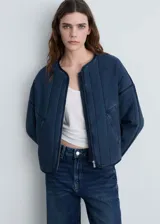 Chaqueta azul de estilo tejano vaquero con diseño acolchado y relleno. Tiene cuello redondo, cierre de cremallera frontal, dos bolsillos de ribete delanteros y mangas largas.