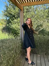 Vestido corto negro de lino, con escote en V, botones frontales y mangas largas acampanadas con volados.