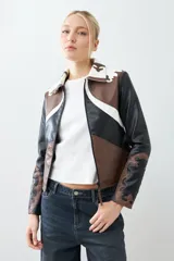 Chaqueta corta de cuero sintético color negro, marrón y blanco, con cuello de piel sintética blanca, cierre frontal con cremallera y bordados en las mangas.