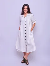 Vestido camisero largo de lino color beige, con cuello clásico, manga larga con puños abotonados y cierre frontal con botones. Tiene un bolsillo de parche en el pecho.