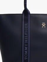 Bolso tote azul marino de poliuretano con cierre de cremallera, doble asa superior con inscripción de Tommy Hilfiger y logo TH dorado en el frente.