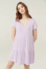 Vestido corto lila con cuello en V y mangas cortas. Tiene corte holgado y dos volados en la falda.
