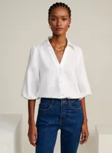 Camisa blanca de lino con cuello alto, escote en V, mangas 3/4 con volumen abullonado y puños elásticos.