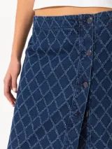 Pollera midi de denim azul con diseño de rombos desflecados, corte recto, tiro alto, abertura frontal con botones metálicos y botón interno de seguridad.