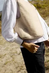 Chaleco corto confeccionado en tejido de textura tipo corderito color beige, con cuello redondo y terminaciones ribeteadas.