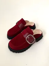 Zueco tipo mule negro, confeccionado en cuero vacuno, con puntera cuadrada y suela track gruesa. Presenta una faja ancha con hebilla metálica plateada sobre el empeine.