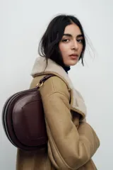 Bolso de hombro ovalado negro con asa de doble tira redonda con detalles metalizados dorados. Cierre imantado y asa de bandolera extraíble con tejido a contraste. Bolso interior con cierre mediante cremallera metálica.