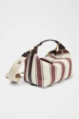 Bolso de mano tipo city, confeccionado en tejido con estampado de rayas verticales en tonos crudo y bordó. Tiene doble correa de hombro extraíble en contraste de tejidos, detalles metálicos y cierre mediante cremallera.