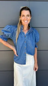 Camisa celeste de mangas cortas abullonadas, cuello mao y cierre frontal con botones.