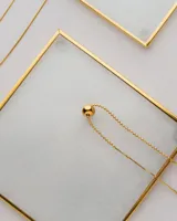 Collar asimétrico dorado con cadena de bolitas y dije esférico.
