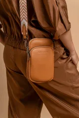 Bandolera pequeña tipo 'phone bag' de símil cuero color rosado pálido, con cierre de cremallera y correa ancha de tela con diseño de chevron en tonos claros.