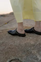 Mules de cuero negro con punta cuadrada y detalle de tachas plateadas en el borde superior.