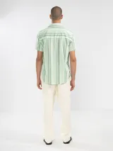 Camisa de manga corta a rayas verticales azules y blancas, con cuello clásico, corte cuadrado y calce relajado. Presenta botones de coco con logo y parche distintivo de Polonio. Confeccionada en Italia con mezcla de lino y algodón.