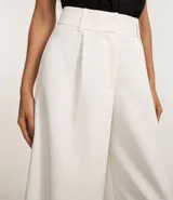 Pantalón pantalona de corte sastrero color blanco, confeccionado en poliéster y elastano, con cintura ancha con trabillas y pliegues delanteros.