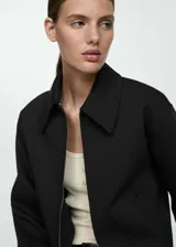 Chaqueta negra con cuello camisero, cierre frontal con cremallera, forro interior y diseño oversize.