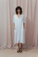 Vestido camisero largo blanco, de manga corta y cuello camisero. Presenta abotonadura frontal completa y bolsillos laterales.