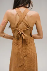 Vestido largo color ocre con estampado de hojas, escote halter cruzado y falda acampanada con volantes.