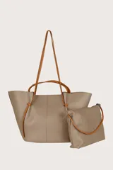 Bolso tote grande color gris topo, con textura granulada y doble asa: una corta al hombro y otra larga para llevar cruzado. Cierre superior con cordones de cuero marrón anudados a los laterales.