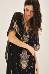 Vestido largo negro de gasa traslúcida bordada con canutillos, lentejuelas y mostacillas. Tiene escote en V, mangas amplias de largo irregular, gancho oculto en el escote y viso al tono con breteles regulables y puntilla en el escote.