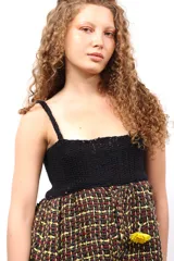 Top con parte superior de crochet negro y parte inferior de tejido plano de telar con diseño a cuadros en tonos amarillo, rojo y negro.