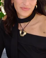 Collar con dije dorado irregular con agujero central, colgando de cordón negro ajustable.