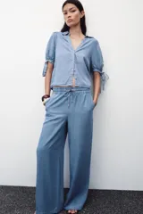 Pantalón celeste de tiro alto con cintura elástica ajustable con cordones, bolsillos delanteros y traseros, y pernera ancha.