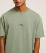 Remera verde salvia de corte relaxed, confeccionada en algodón más sostenible. Presenta cuello redondo, mangas cortas y estampa frontal con lettering y árboles.