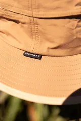 Sombrero tipo pescador color beige con ala ancha, cordón ajustable y parche con logo de la marca Denali.