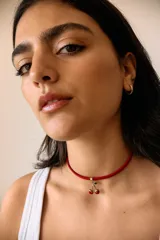 Gargantilla con cordón rojo y dije de cerezas rojas con detalles dorados y hojas verdes.