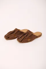 Zueco de cuero gamuzado color marrón, con punta cuadrada y detalle de gran borla de flecos en el empeine. Presenta aberturas laterales y suela plana.