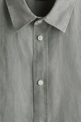 Camisa de lino color gris con cuello inglés, tapeta clásica, canesú en la espalda, mangas largas con tapeta de manga y botón, cierre ajustable de botón en los puños y bajo redondeado.