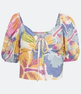 Top cropped de tejido tipo laise con estampado floral pixelado en tonos pastel (rosa, amarillo, azul, blanco). Presenta escote corazón con abertura central y lazo ajustable, y mangas cortas abullonadas.