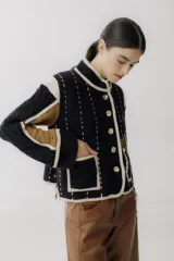 Chaqueta corta de lana color negro con detalles en beige y marrón. Tiene cuello mao, cierre frontal con botones y bolsillos de parche.