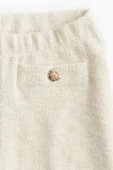 Pantalón ancho color crema en tejido bouclé con elástico en la cintura y bolsillos decorativos con botón dorado.