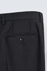 Pantalón de vestir negro de corte relaxed fit confeccionado en tejido con lana. Cuenta con bolsillos frontales y traseros de doble vivo con botón. Cierre frontal con cremallera y botón.